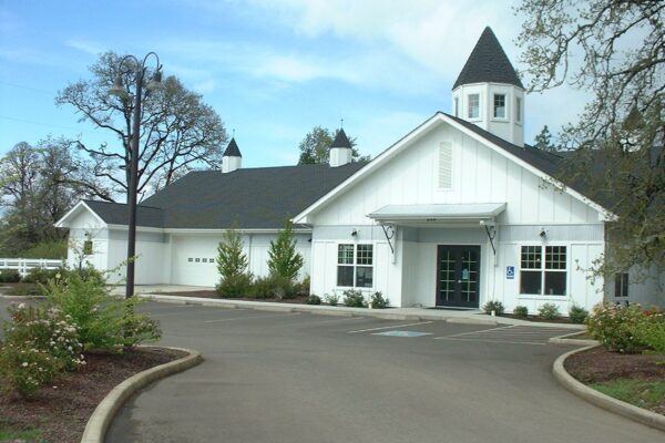 White building with cupola and landscaped exterior - Creswell Veterinary Clinic  Alt Text: Wide shot of a white veterinary clinic with a dark pitched roof, central cupola, and landscaped entrance, set against a blue sky with scattered clouds - Creswell Veterinary Clinic